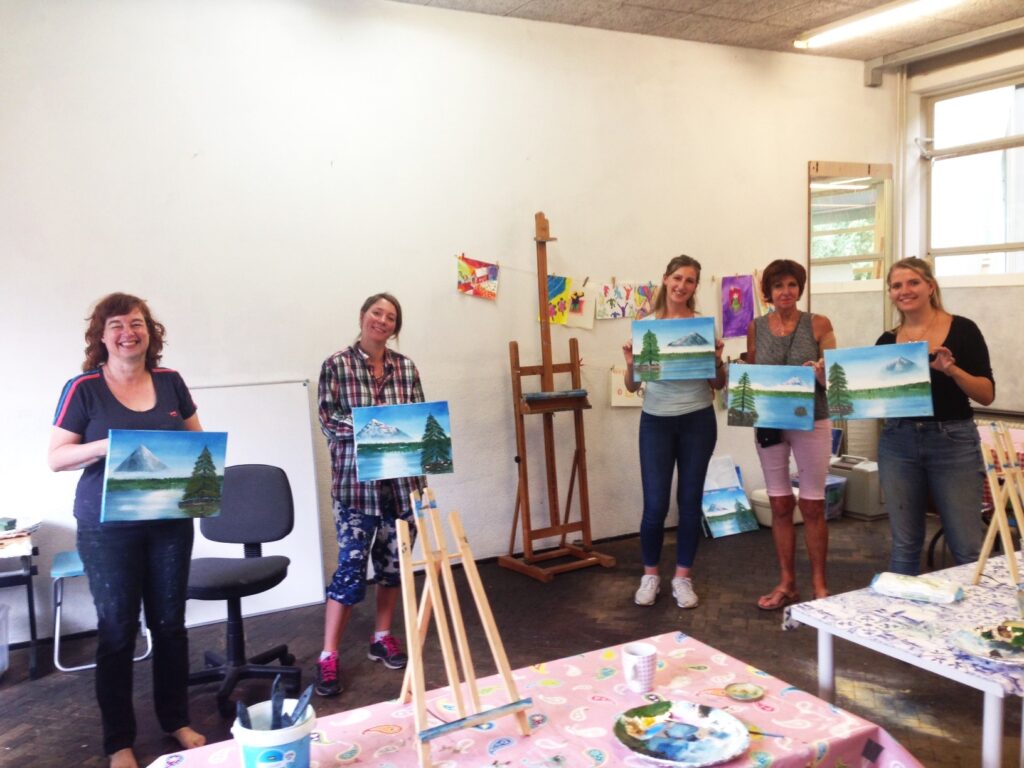 deelnemers aan een bob ross schilderworkshop laten hun werk zien